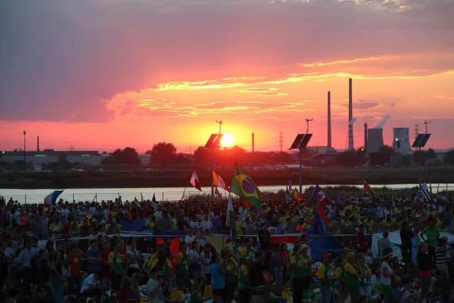 Multidão de jovens católicos celebra a Jornada Mundial da Juventude com bandeiras e alegria num ambiente de partilha.