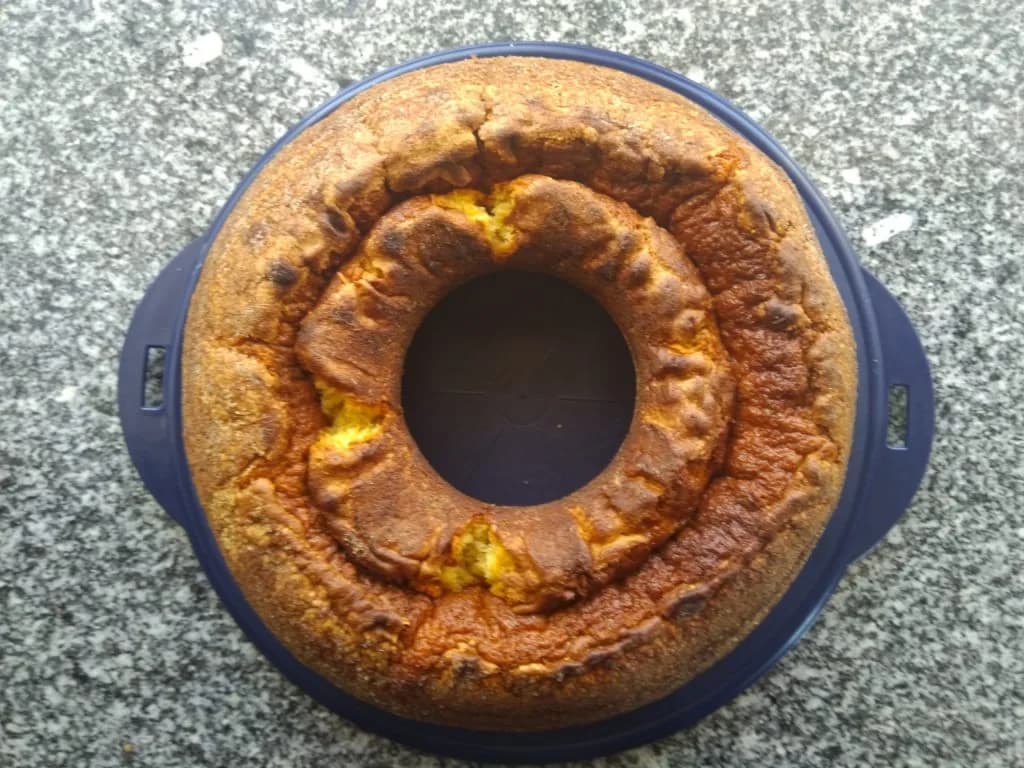 Um bolo de natas dourado e fofo, acabado de sair do forno, dentro de uma forma redonda untada e polvilhada.