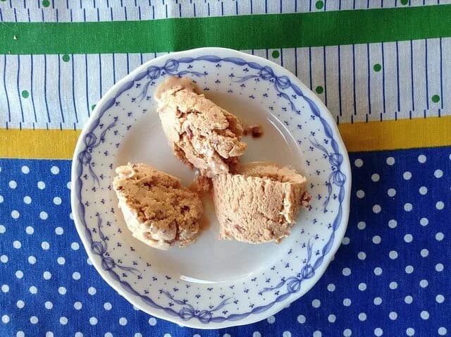 Taça com bolas de gelado de cereja caseiro, com cerejas frescas por cima, num ambiente rústico.