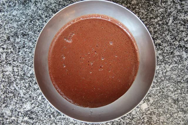 Taça de vidro com mousse de chocolate caseira polvilhada com raspas de chocolate sobre uma mesa de madeira.