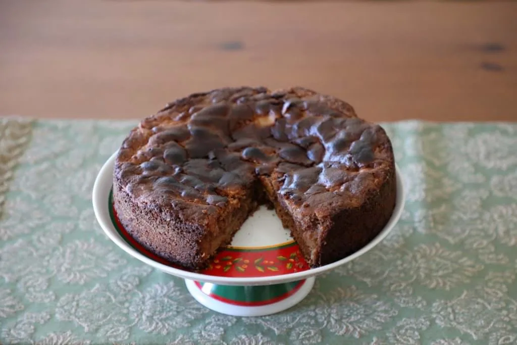 Bolo de maçã dourado servido num tabuleiro, decorado com fatias de maçã em meia-lua e frutos secos.