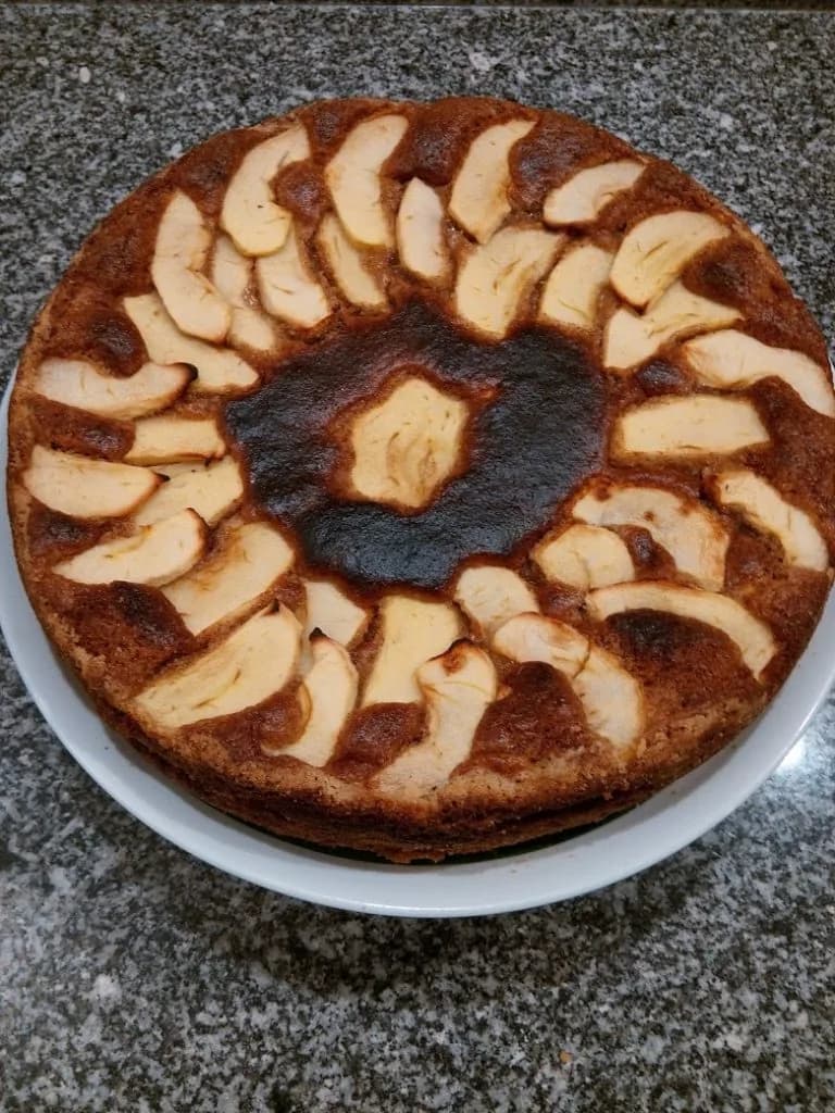 Bolo de maçã caseiro acabado de cozer num tabuleiro, decorado com fatias de fruta e frutos secos.