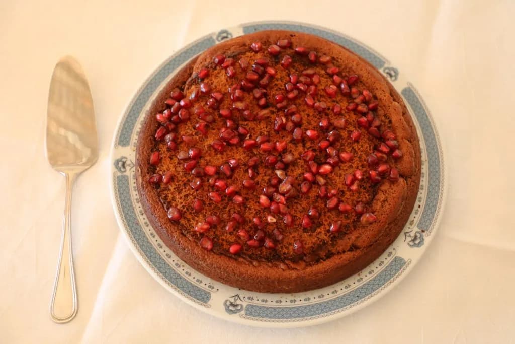 Um delicioso bolo de mel caseiro decorado com gomos frescos de romã sobre um prato de serviço.