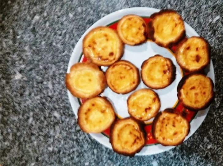 Vários pastéis de nata caseiros com massa crocante e recheio dourado polvilhados com canela e açúcar.