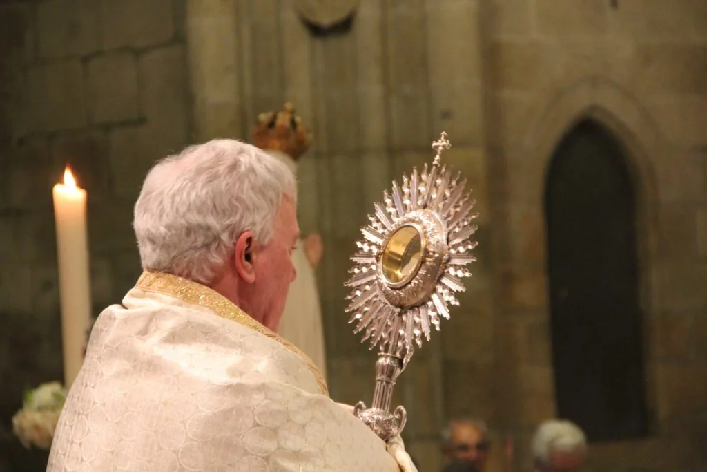 Fiéis em procissão solene do Corpo de Deus pelas ruas decoradas com flores e colchas.