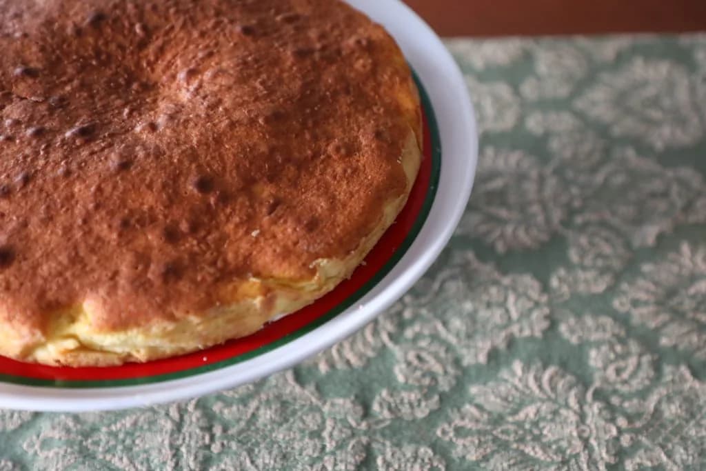 Tarte de requeijão caseira acabada de sair do forno, servida num prato sobre uma mesa de madeira.