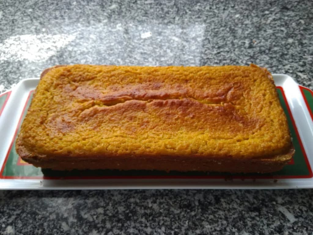 Fatia de bolo de meloa caseiro servido num prato branco sobre uma mesa de madeira.